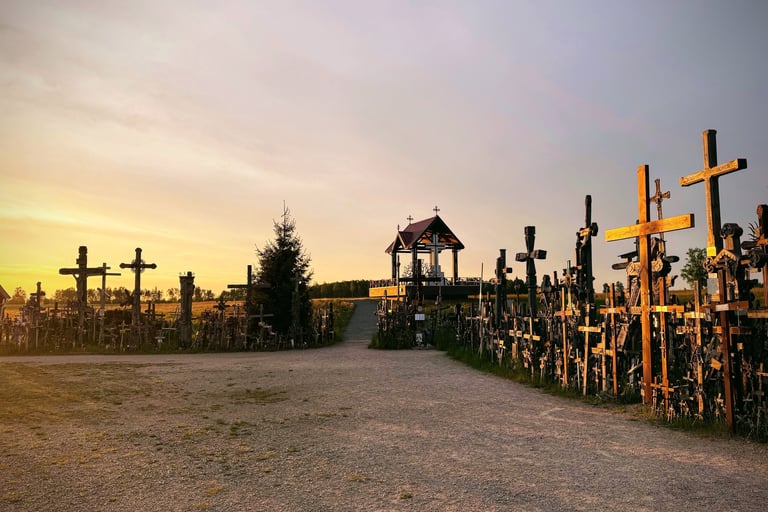 Hundreds of wooden crosses stand at the Hill of Crosses in Lithuania during a golden sunset.