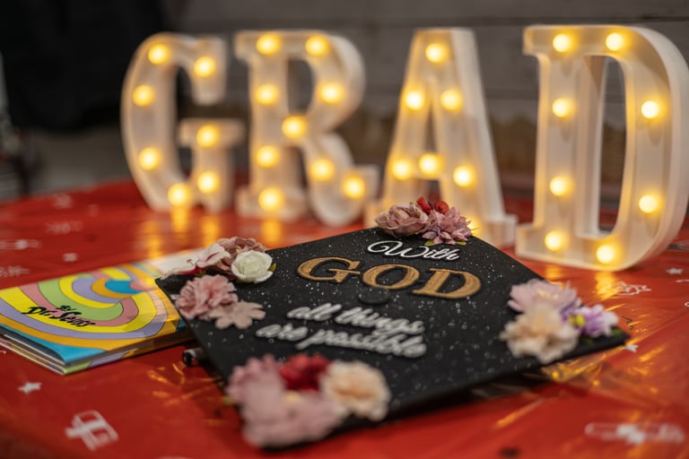 Graduation cap laying on table with the word GRAD lit up behind it.
