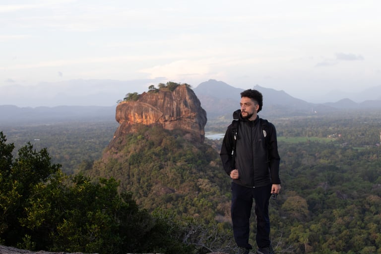 A man standing on a mountain, posing in front of Sigiriya Rock (Sri Lanka), in the background. Beautiful landscape with trees