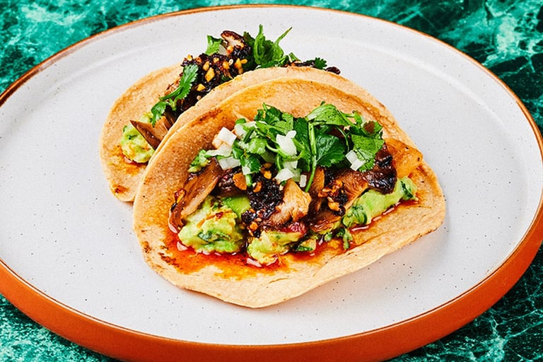 two vegan tacos on a plate with a green table cloth