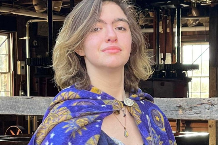 teenager with brown and blond shoulder-length hair wearing a celestial cape and a proud expression