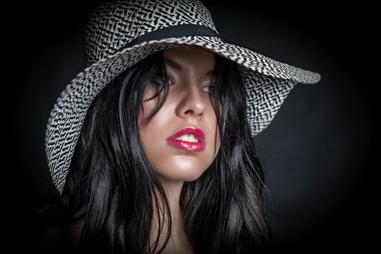 Porträt einer Frau mit schwarzem Haar und breitem Hut, aufgenommen im Studio mit dunklem Hintergrund – professionelles Beauty