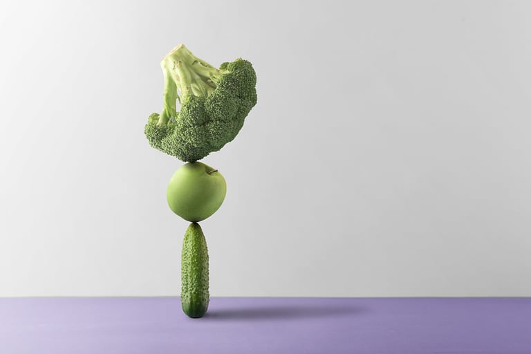 a head of broccoli balanced on a green apple and pickle balanced on a green cucumber