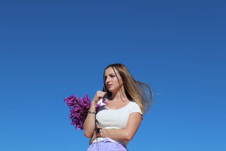 Photo of Audra Baruch underneath a sky holding purple flowers