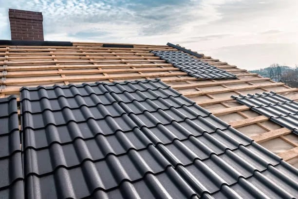 Professional installation of black metal roof tiles on a residential wooden frame structure.