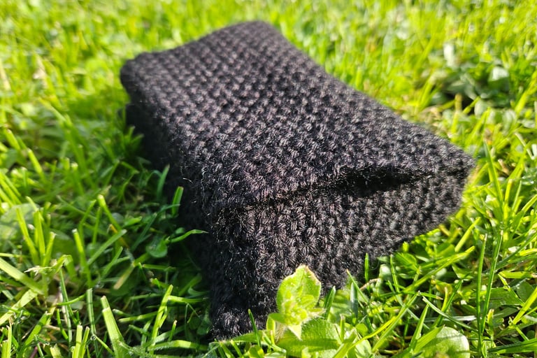 Handmade black crochet tarot card pouch protecting tarto cards on a sunny grass lawn with daisies.