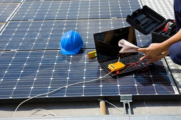 A technician performing maintenance and diagnostic testing on rooftop solar panels with a laptop.