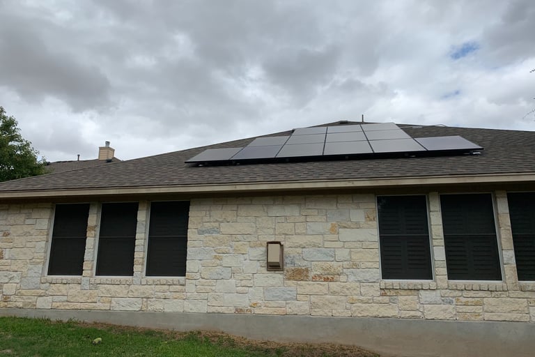 Residential rooftop solar panels installed on a stone house under a cloudy sky.