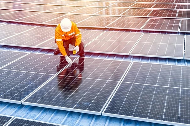 A technician in a hard hat installing solar panels on a rooftop for renewable energy.
