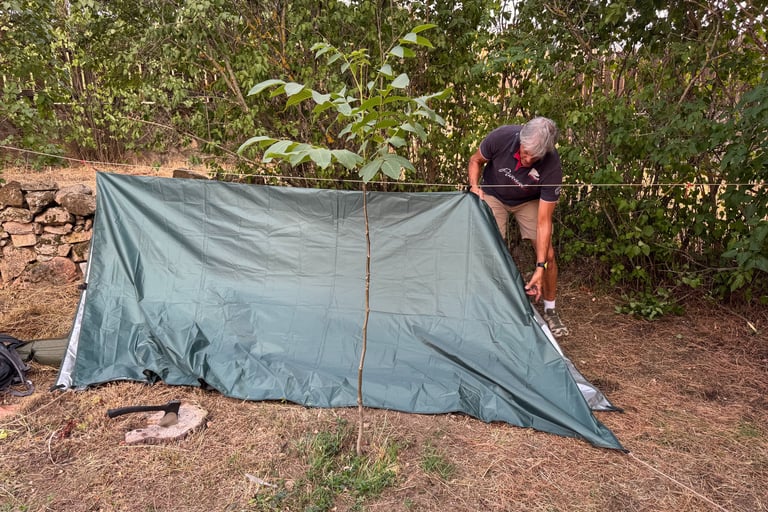 una persona construyendo un refugio de fortuna con un tarp suspendido de una linea de cordino