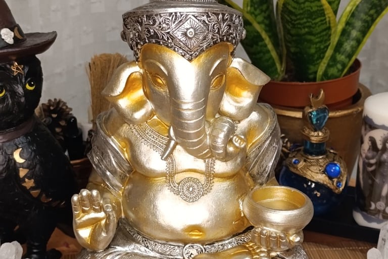 La foto muestra una figura decorativa de Ganesha en colores plata y oro