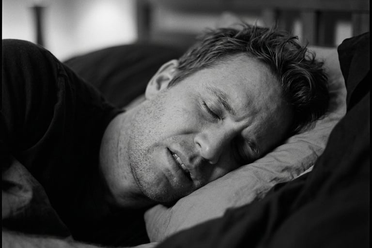 A man experiencing restless sleep or a nightmare while lying in bed, captured in a black and white close-up.