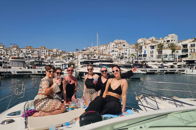 girls raising glasses at the yacht´s bow. Puerto banus marina behind clear blue day