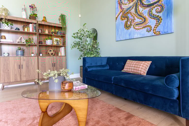 Modern reception room featuring a navy blue velvet sofa, wooden bookshelf, and glass coffee table.