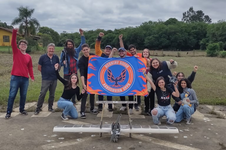 Membros da equipe segurando a bandeira e com mãos erguidas, atrás do avião de 2023