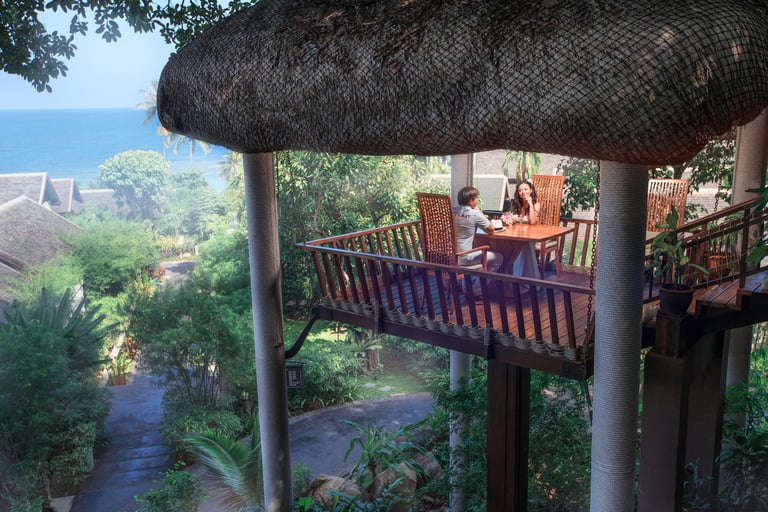 A couple having a romantic dinner in a treehouse-style balcony overlooking tropical greenery