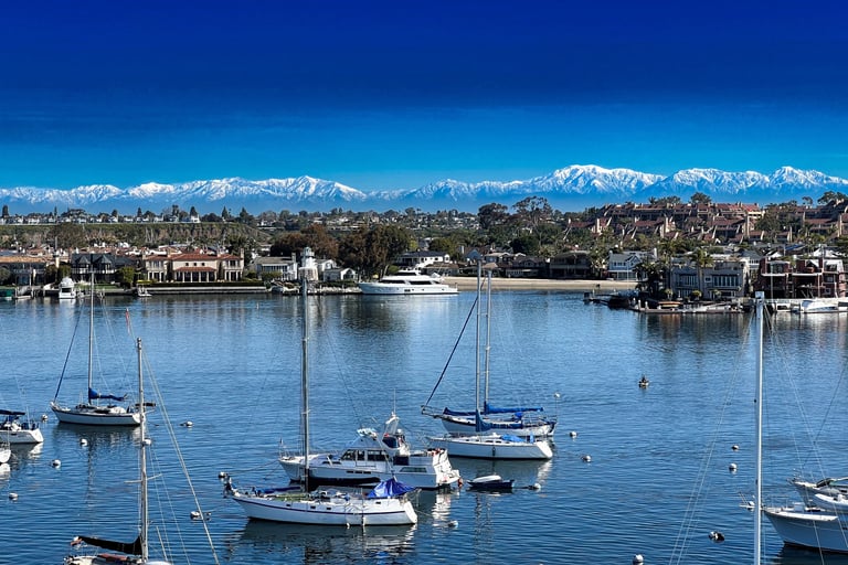 Newport Harbor with sailboats in the foreground and snow-covered mountains visible in the distance.