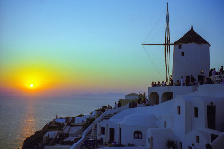 Sunset over the Aegean Sea, with whitewashed buildings and a windmill in the foreground.