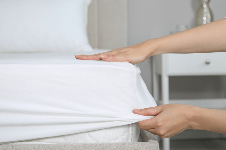 a person holding a bed with a white sheet covering it - fitted sheet