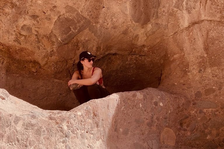 A woman hiker sits in an Arizona red rock desert cave formation during a canyon trek.