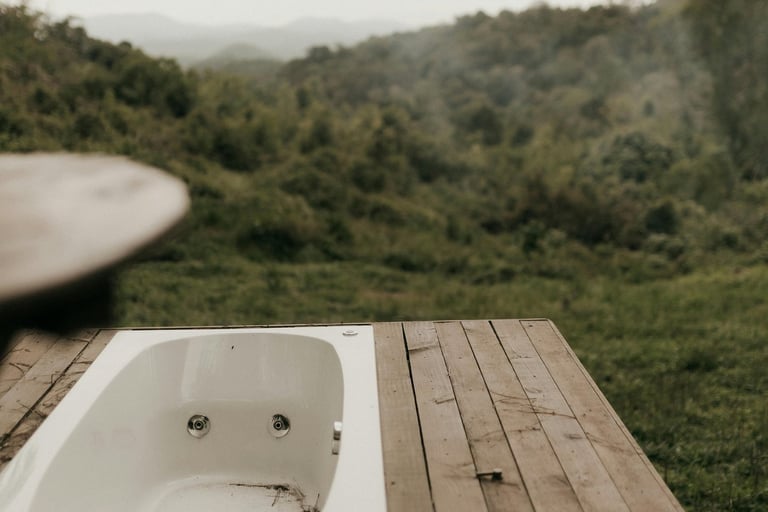 A modern outdoor bathtub built into a wooden deck overlooking a lush green valley and mountains.