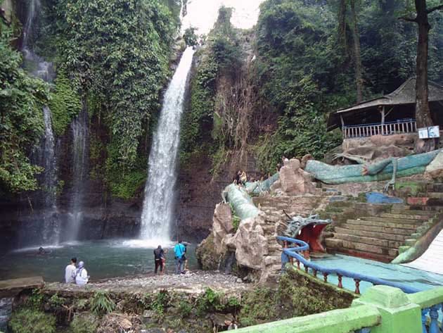 Air terjun ganda Curug Luhur Bogor mengalir deras di antara bebatuan besar, dilengkapi dengan kolam renang buatan (waterpark)