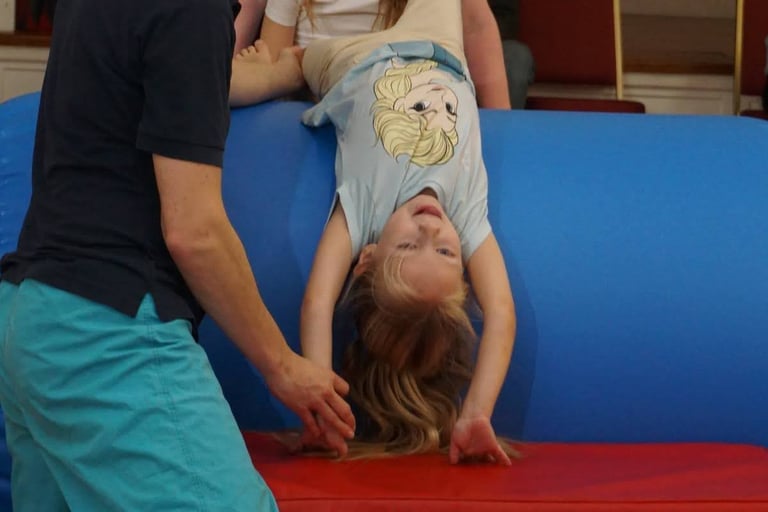 a young girl is upside down in a SEND gymnastics session with coach support