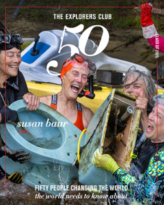 Susan Baur with three other women, cheering as they pull up a dirty blue toilet from the water. 