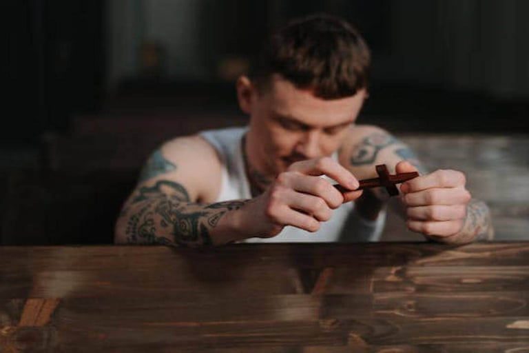 A man with tattoos on his arm, kneeling and holding a small cross