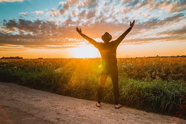 a man standing on a dirt road with his arms up in the air