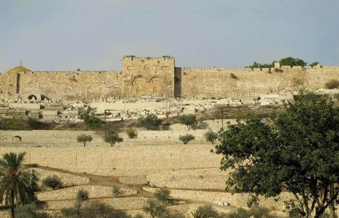 Sealed Golden Gate in Jerusalem’s eastern wall, viewed from a terraced foreground with trees.