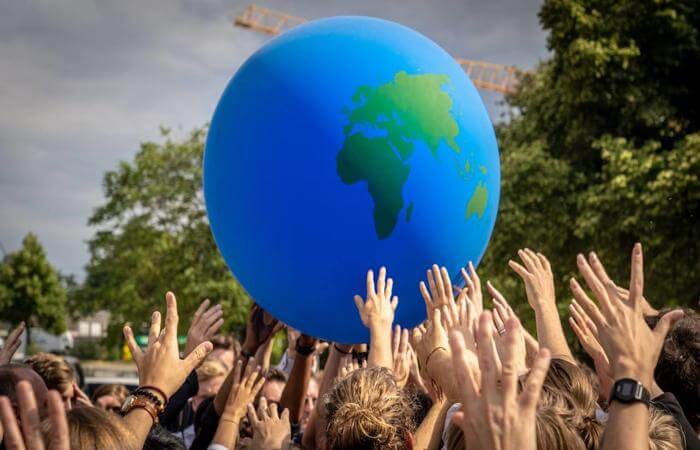 Group of people lifting a globe together, symbolizing unity and global care.
