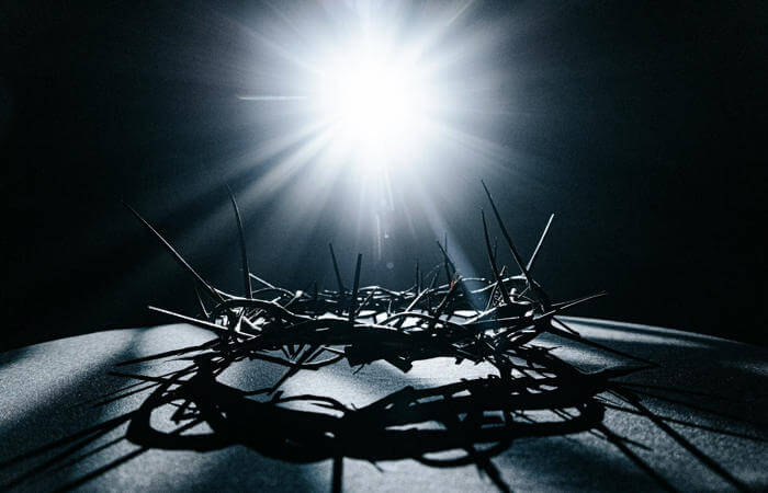 Crown of thorns on a dark surface illuminated from above, casting dramatic shadows and light.