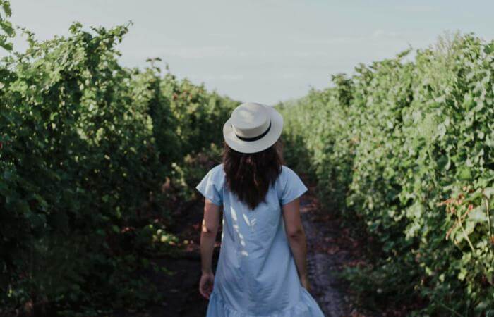 a woman in a white dress and hat walking down a path