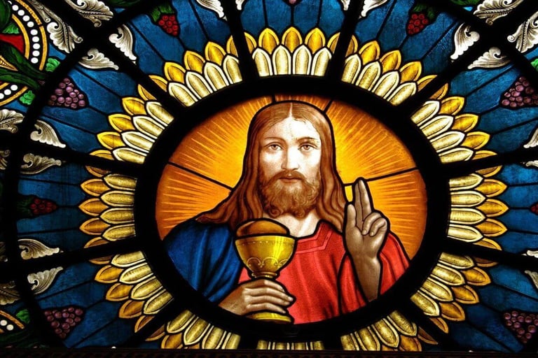 Stained glass window showing Jesus with a chalice and blessing gesture, surrounded by vibrant symbol
