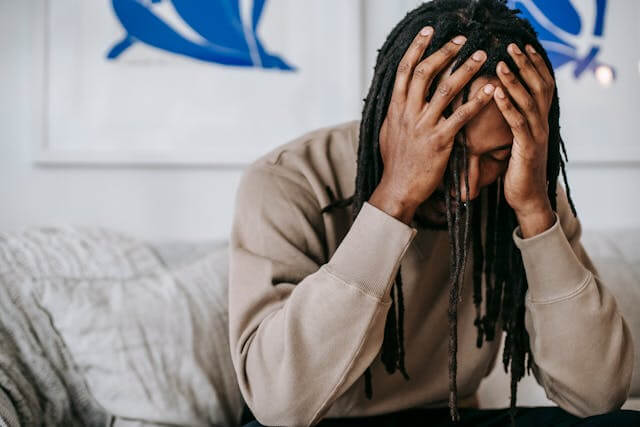 a man with dreadlocks sitting on a couch with his hands on his head