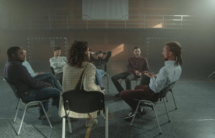 Seven people seated in a circle indoors, engaged in group conversation or reflection.