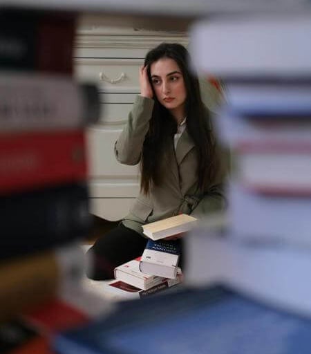 Individual reading a book, viewed through a tunnel of stacked books in a cozy indoor setting.