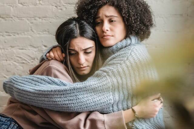 a woman in a sweaterless sweater is hugging a friend with compassion
