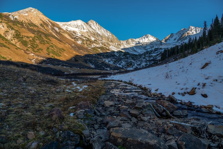 Beautiful snow-dressed high mountain peaks shine above Rustlers Gulch during fall sunset