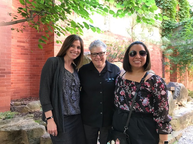 three women standing next to each other in front of a brick building