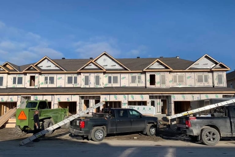 New multi-family townhouse construction project with house wrap, pickup trucks, and heavy equipment.