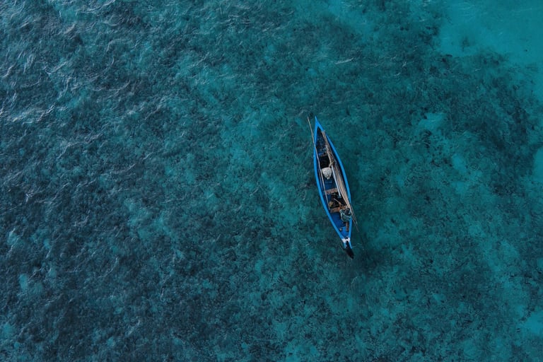 Aerial view of a small blue boat floating on the clear turquoise waters of Rodrigues Island