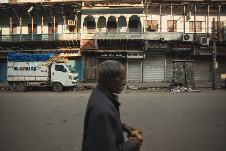 Man walking past closed shops and old façades on a quiet Old Delhi street.
