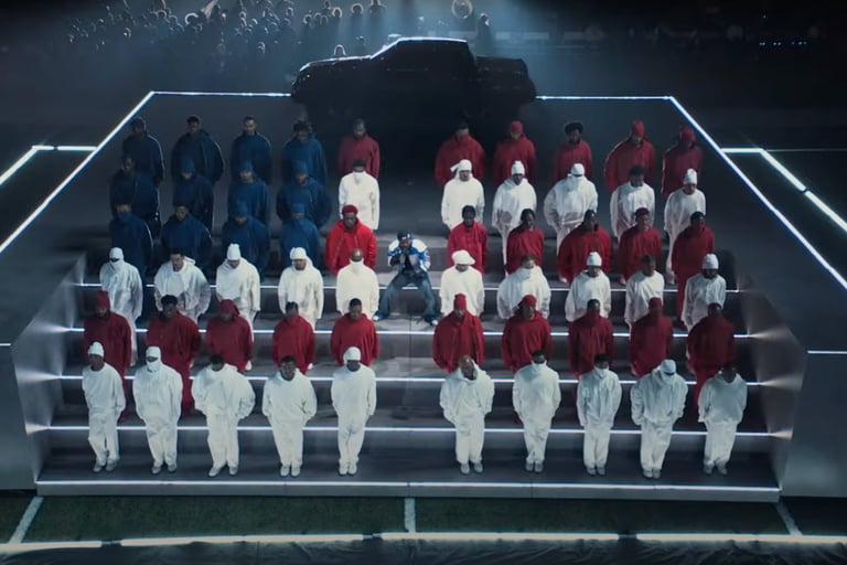 Kendrick Lamar performing in the middle of a group of people wearing red white and blue in the pattern of the American flag.