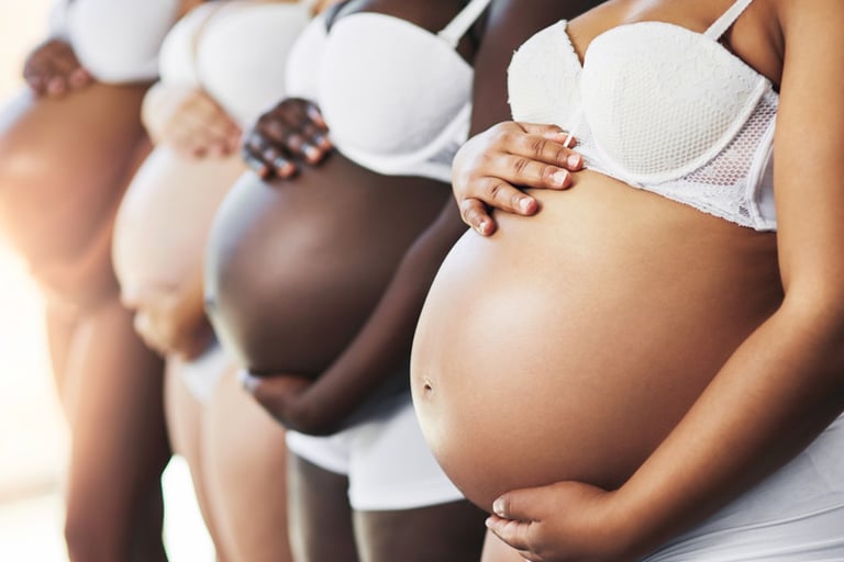 Diverse group of pregnant women standing in a row cradling their bellies.