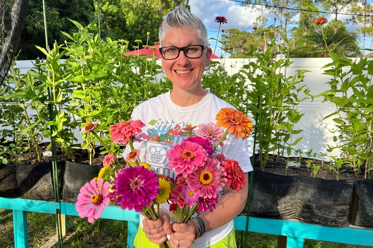 Steph holding zinnias standing in front of a raised cut flower bed