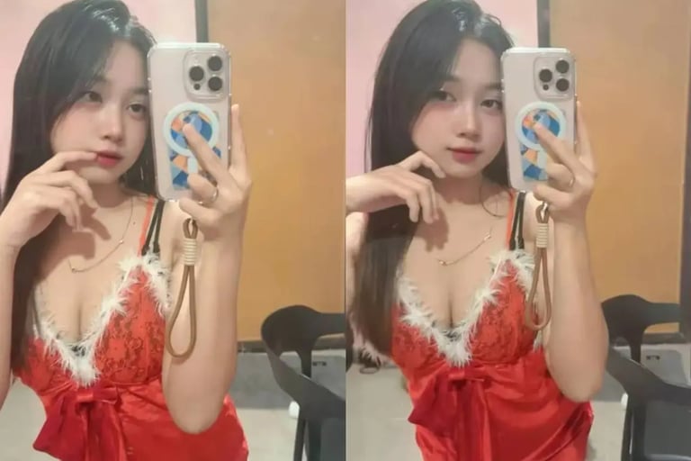 A young woman taking a mirror selfie wearing a red lace holiday-themed lingerie set with white fur trim.