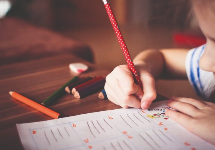 Main d'un enfant tenant fermement un crayon à pois rouges, s'appliquant à un exercice d'écriture, une technique encouragée pa