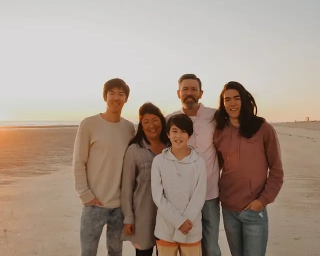 interracial caucasian and asian family with 2 teenage boys and 1 preteen boy at sunset smiling on the beach